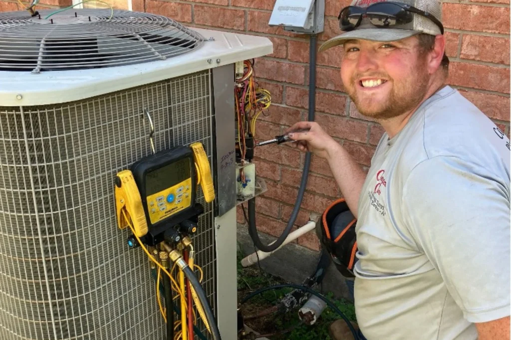 Complete Care Plumbing Electric & AC technician inspecting and repairing an outdoor air conditioning unit using diagnostic gauges and electrical testing equipment beside a brick wall
