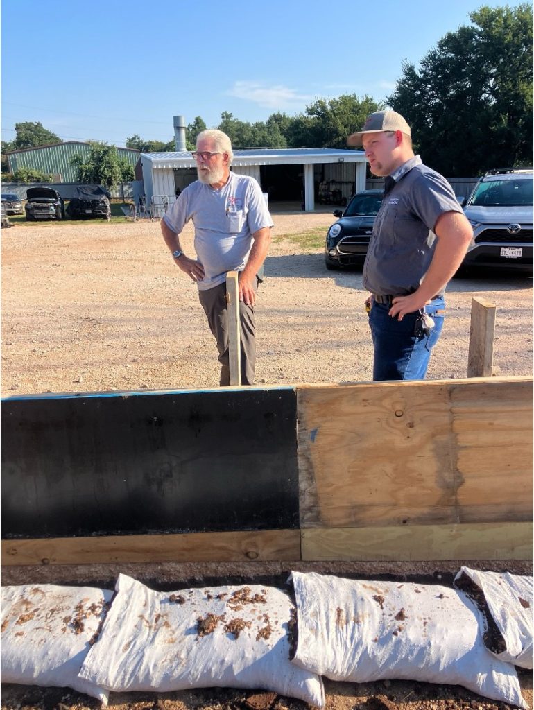 Complete Care Plumbing Electric & AC team technicians discussing a construction and installation project beside a framed work area with sandbags and commercial buildings in the background. 
