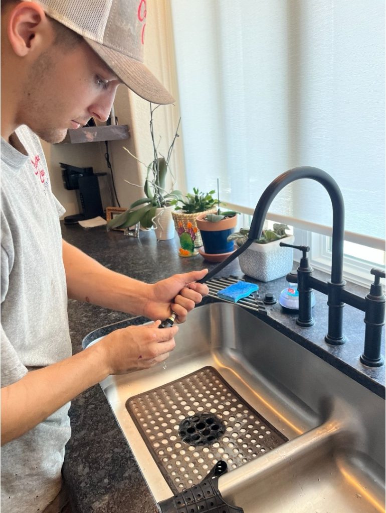 Complete Care Plumbing Electric & AC technician repairing a residential kitchen faucet and sink plumbing system inside a customer's home