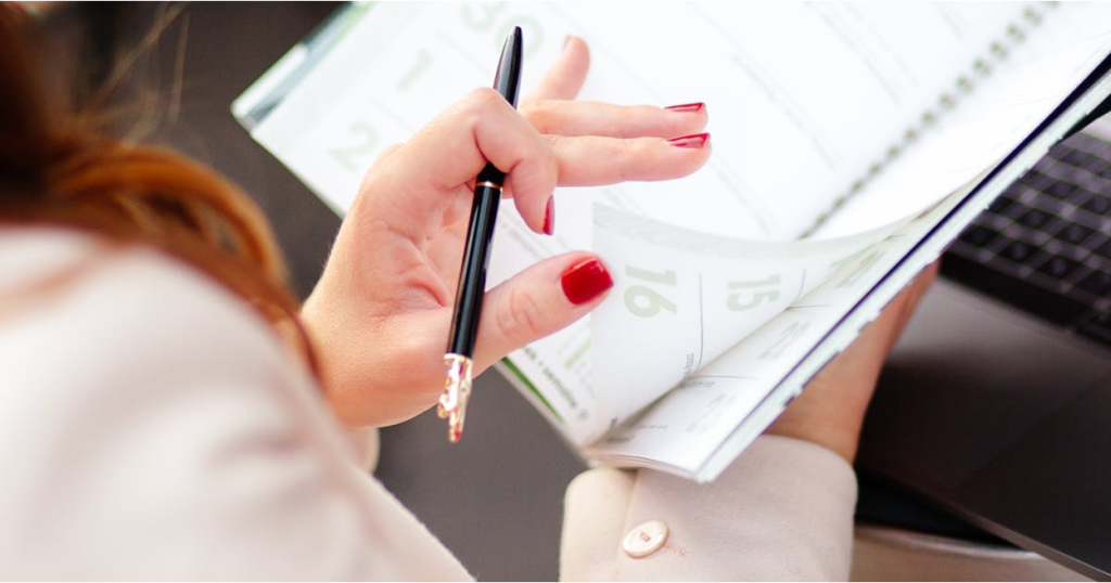 Woman holding a pen over an open desk calendar near a laptop
