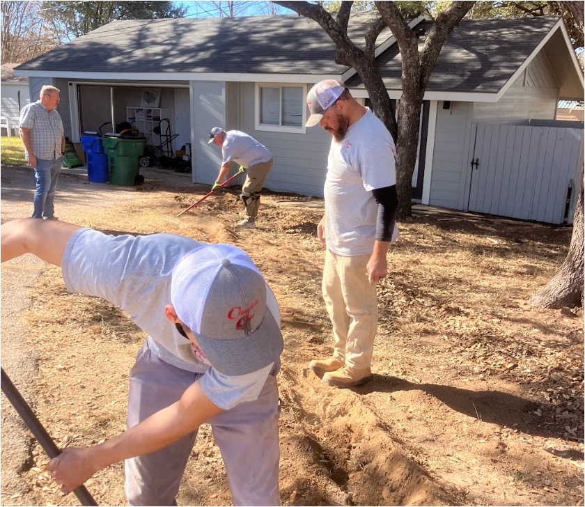 Several men work on landscaping a dirt yard in front of a gray house