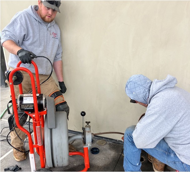 Two professional plumbers working on a sewer machine installation.