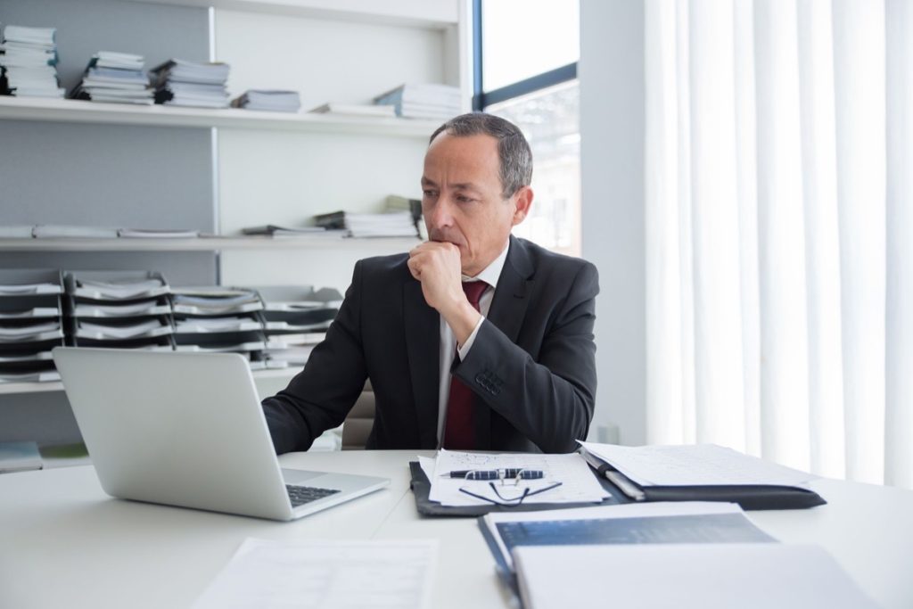 Business owner alone at his desk studying figures on a laptop