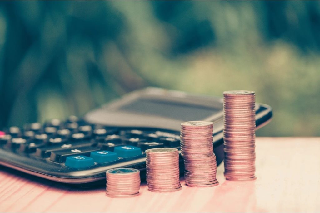 Calculator beside four rising stacks of coins representing business earnings calculations
