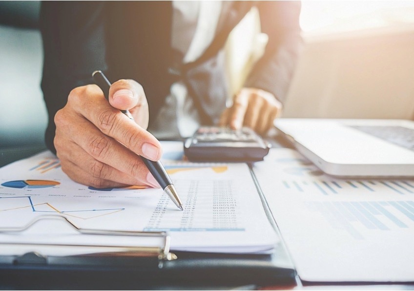 Hands working through figures on a printed financial statement with a calculator.