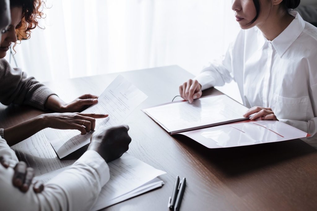 Three people comparing documents across a table while reviewing Adjusted EBITDA adjustments