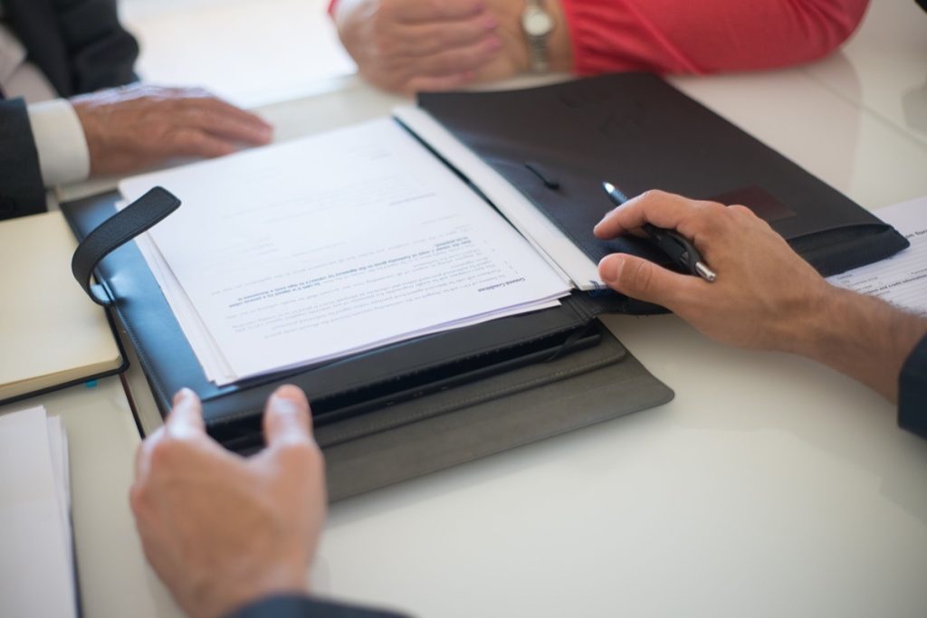Three people reviewing an EBITDA calculation on a printed statement during a meeting