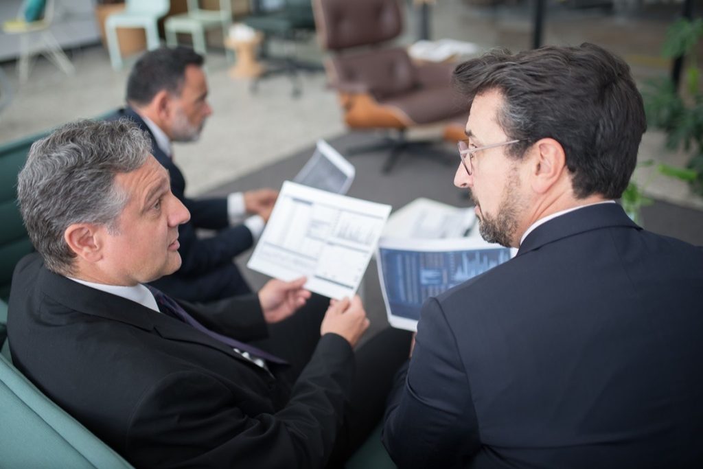Two men discussing a printed financial report in a meeting area