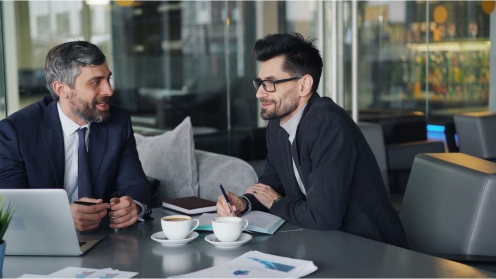 Two men in a meeting discussing which earnings figure applies to a business sale.
