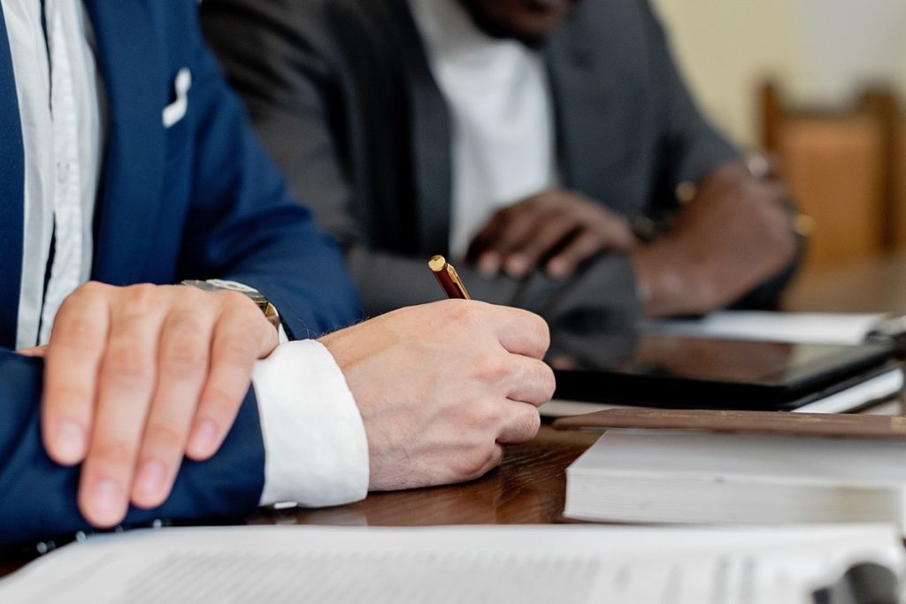 Two men taking notes side by side during a business sale meeting