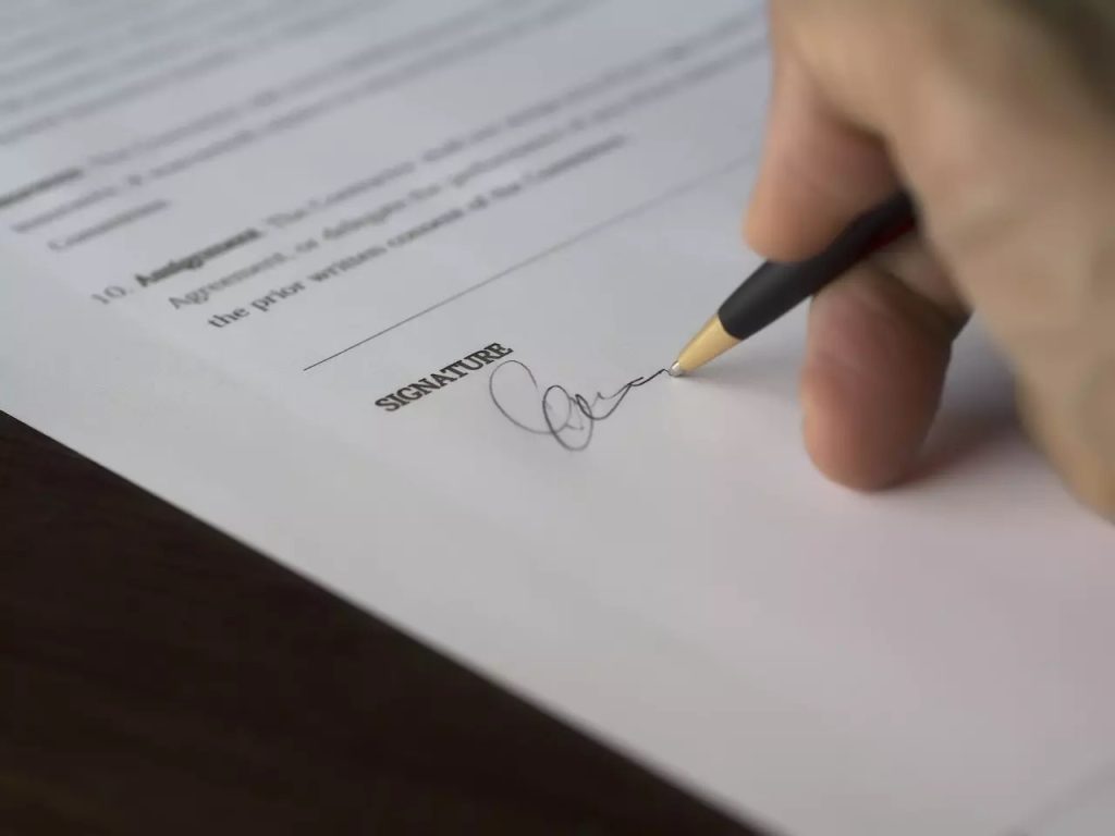 Close-up of a hand signing a formal agreement document with a pen