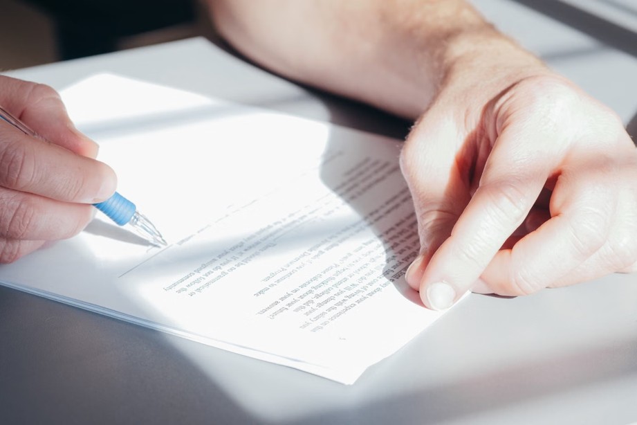 Close-up of a person signing a printed document with a blue pen on a desk