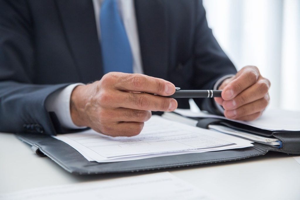 Close-up of hands holding a pen over a document, pausing before signing