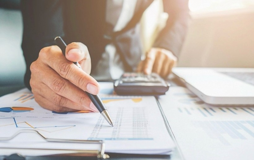 Person reviewing financial spreadsheets and charts while using a calculator at a desk