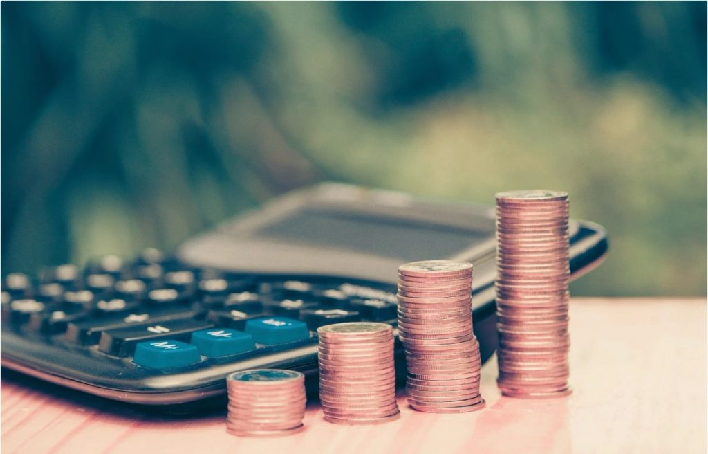 Stacked coins in ascending order beside a calculator on a wooden surface, symbolizing financial growth