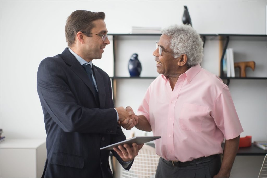 Two men smiling and shaking hands in an office, one holding a tablet