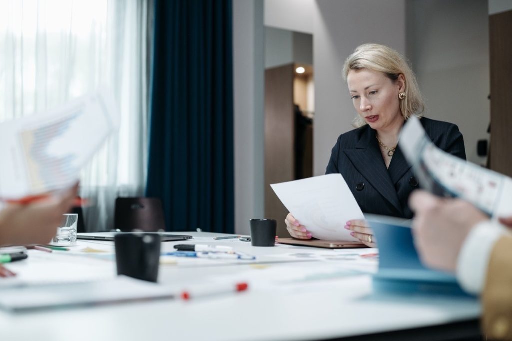 Woman reviewing a printed report while others hold documents around a meeting table