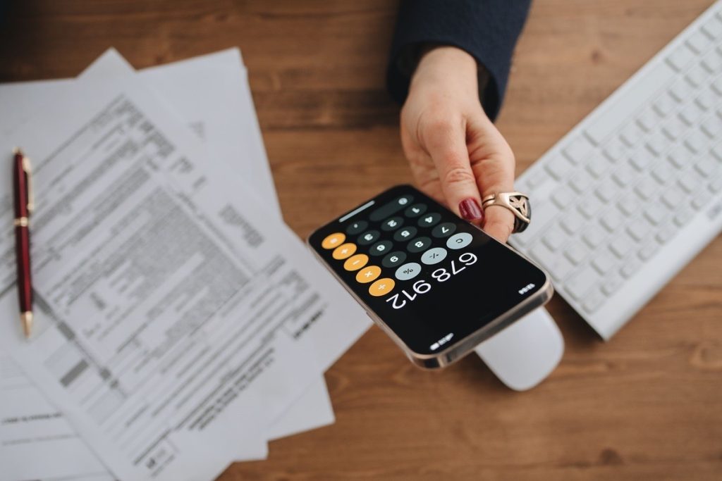 A hand holding a phone calculator over financial documents on a desk