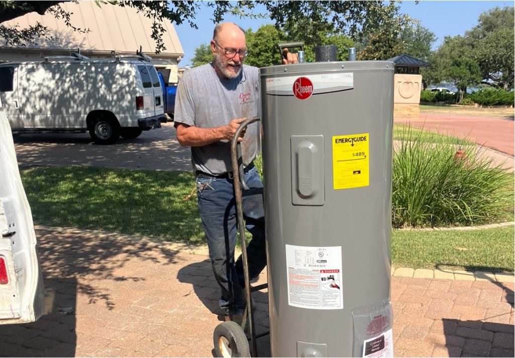 A plumber transporting a Rheem water heater on a dolly at a residential job site