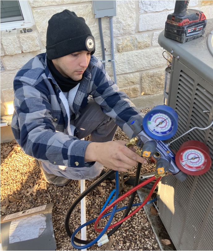 HVAC technician connecting refrigerant gauges to an outdoor condensing unit