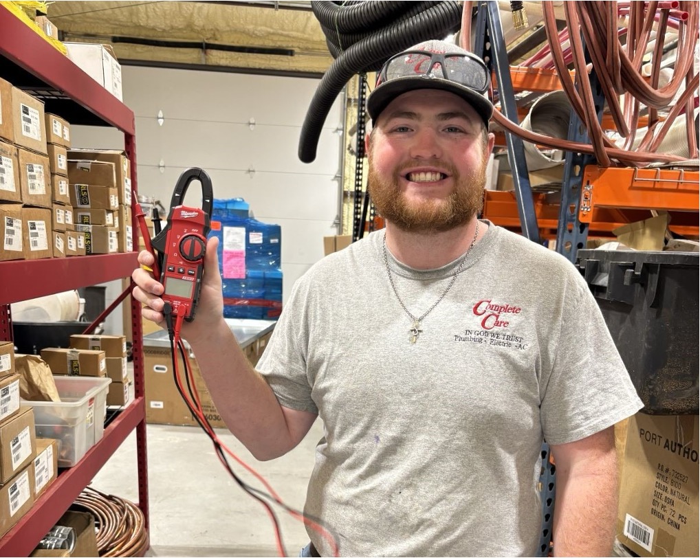 HVAC technician with a clamp meter beside shelves of parts and supplies