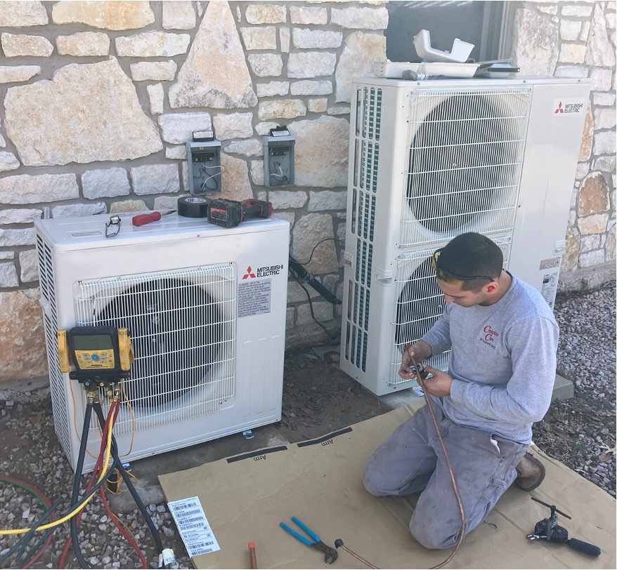 HVAC technician working on two outdoor mini-split units with copper line and tools laid out