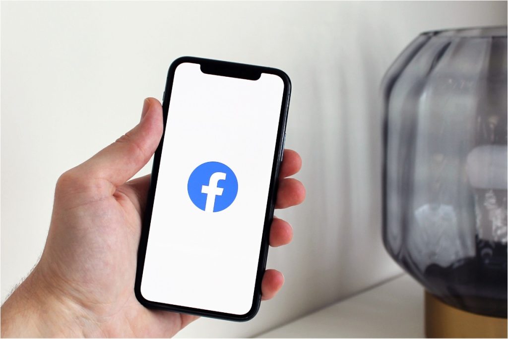 Hand holding smartphone displaying the Facebook logo on a white screen