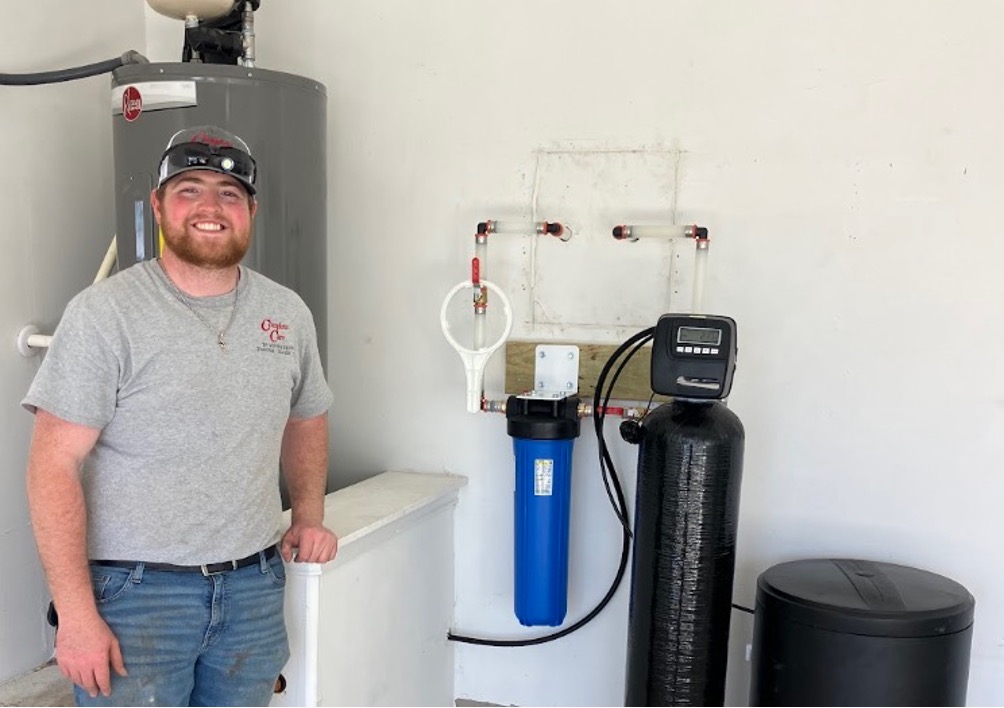 Smiling HVAC technician posing beside a completed water softener and filtration system installation indoors