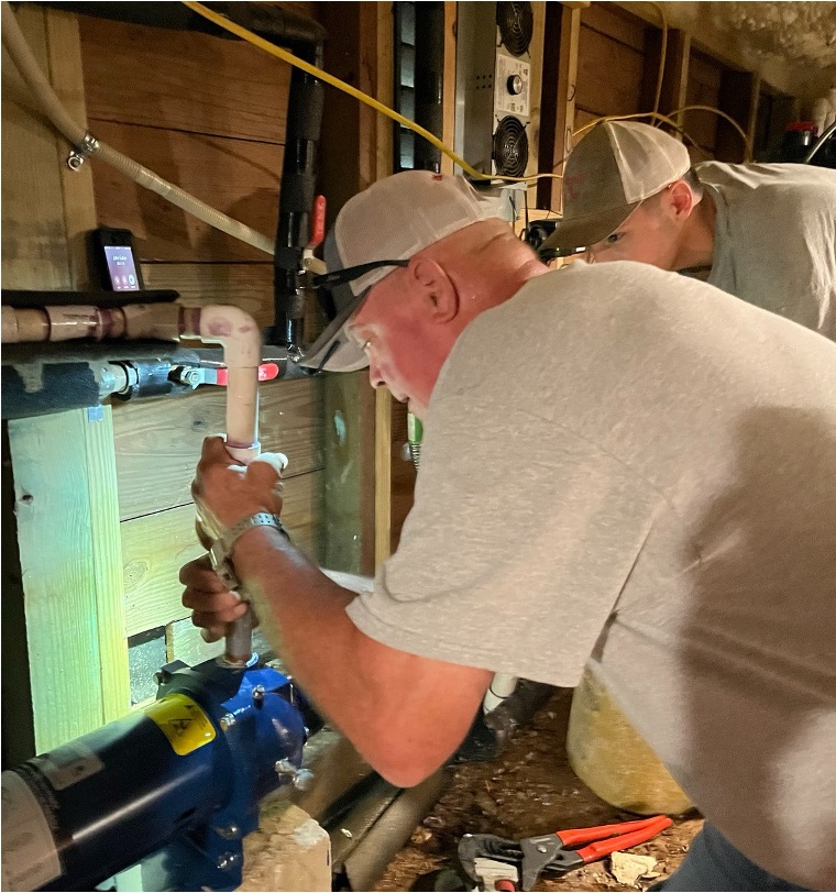 Two plumbing technicians working on pipe fittings in a residential utility area