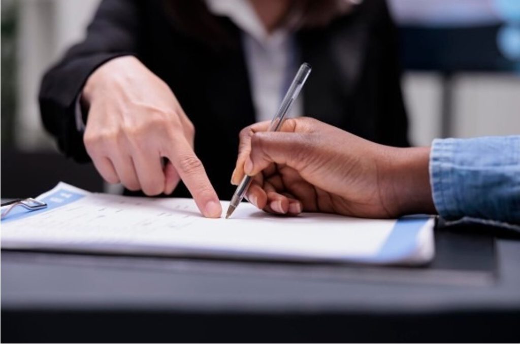 Close-up of two people reviewing and signing a document at a desk