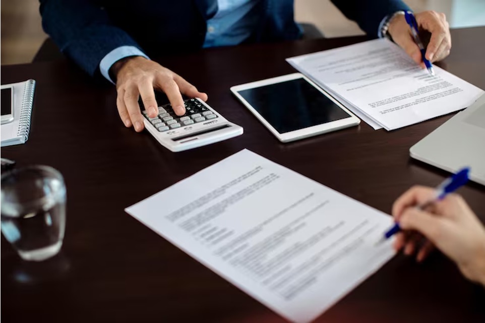 Seller and advisor calculating working capital adjustment figures with a calculator over purchase agreement documents