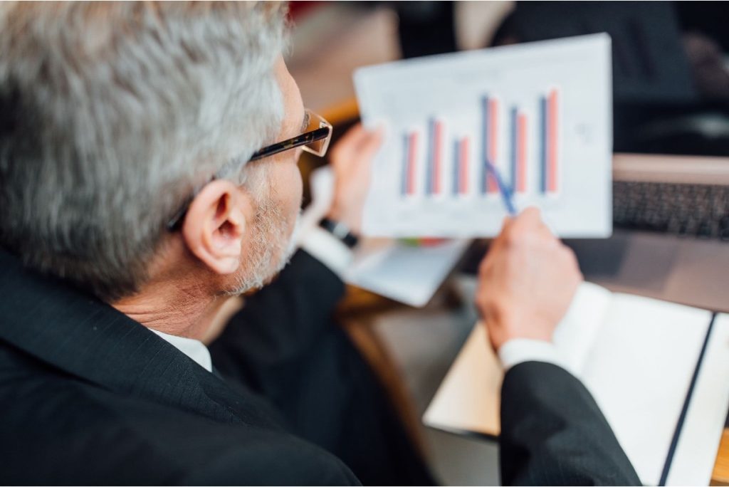 Senior professional analyzing a bar chart on a printed report.