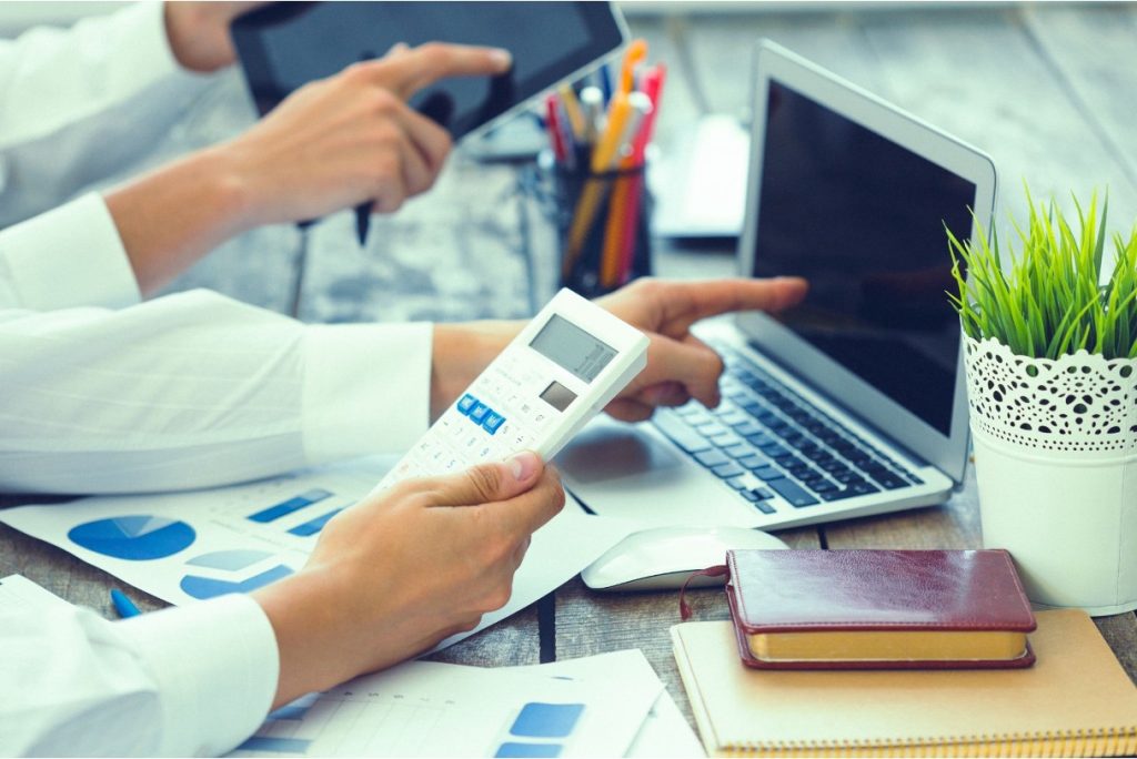 Two colleagues working with a calculator, laptop, and financial documents