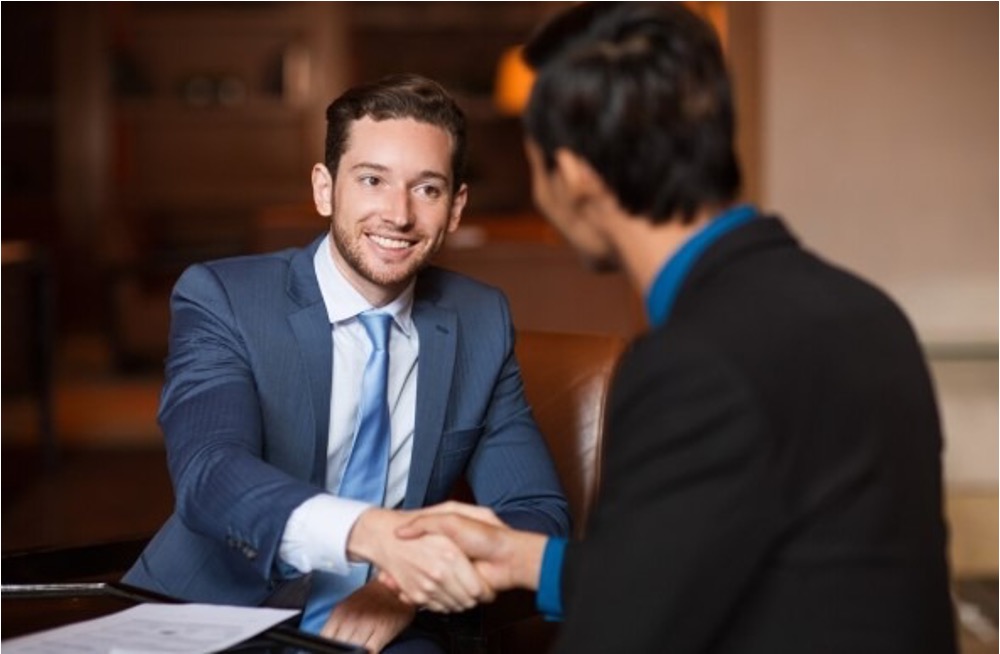 Two professionals in suits shaking hands across a table during a business meeting